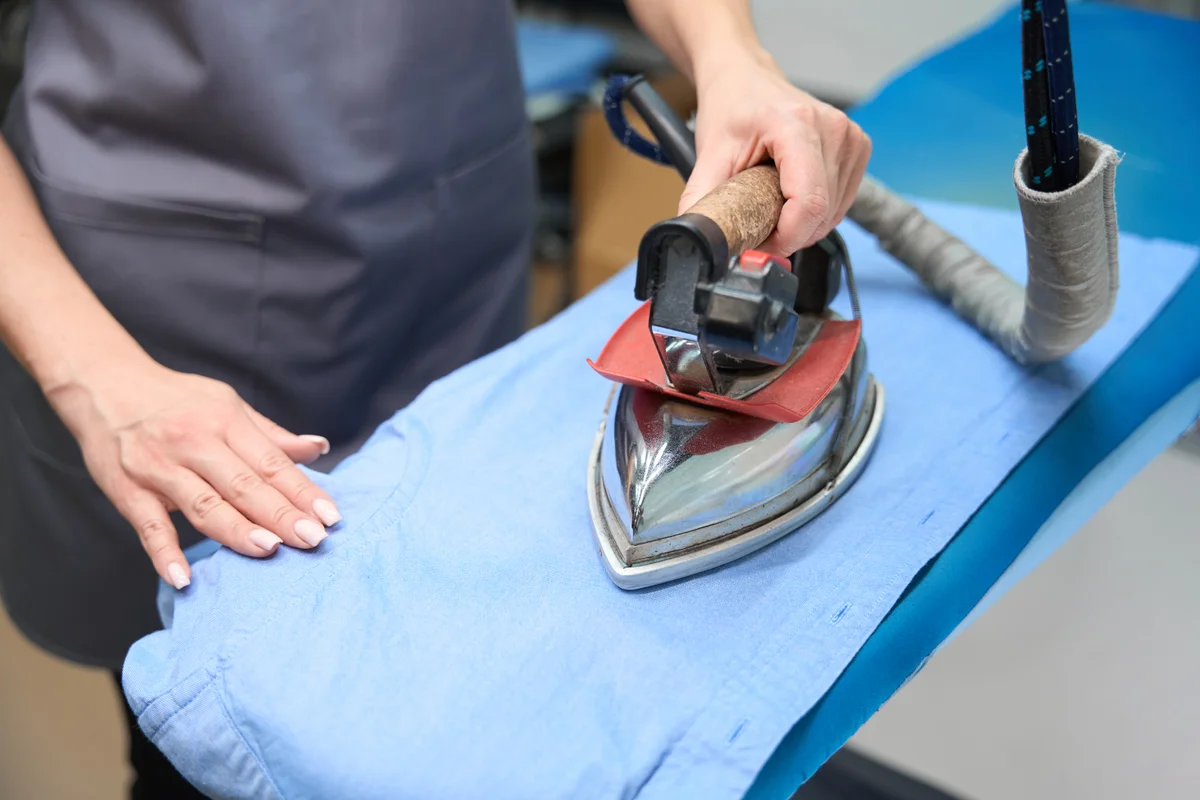 Hands carefully pressing a blue garment during production